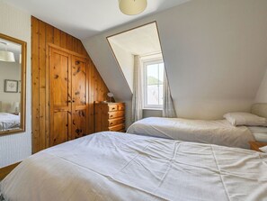 Un dormitorio con techo inclinado, armario de madera, dos camas, un aparador y una ventana con cortinas.