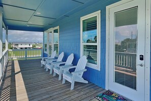 Eine überdachte Veranda mit weißen Adirondack-Stühlen, einer blauen Fassade und Blick auf die Umgebung.