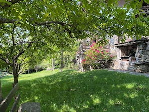 Ein Steinhaus mit Kamin, umgeben von üppigem Grün und Bäumen.