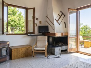 Ein modernes Wohnzimmer mit Kamin, Fernseher und einem großen Fenster mit Blick auf Grünflächen.