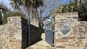 Een stenen muur met een poort en een bord waarop 'Pinecroft' staat.