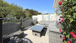 Een terras buiten met rieten meubilair, een poort en een muur vol klimrozen.