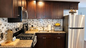 A modern kitchen with dark wood cabinets, stainless steel appliances, and a tiled backsplash. - Welcome to The Woven Nest Near NYC  (Paterson)