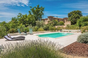 A swimming pool with lounge chairs, surrounded by greenery and a stone building in the background. - A slice of paradise (Rustrel)