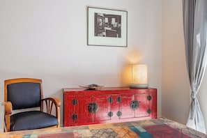 Ein Zimmer mit einem Holzhocker, einem roten Schrank mit Lampe und einem gerahmten Foto an der Wand.