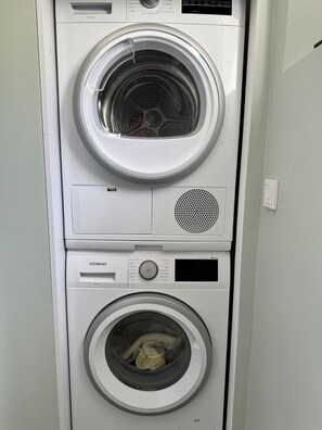 A stacked washer and dryer unit with a control panel, a power outlet, and a vent.