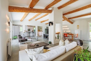 A spacious living area with a high ceiling, wooden beams, a sofa, a coffee table, and a kitchen in the background. - A slice of paradise (Rustrel)