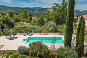 A swimming pool with lounge chairs, surrounded by greenery and hills in the background. - A slice of paradise (Rustrel)