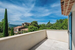A balcony with a view of a village, a clear sky, and distant hills.
