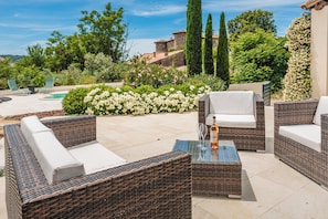 Terrassenmöbel aus Rattan, ein Glastisch und ein Pool inmitten eines Gartens.