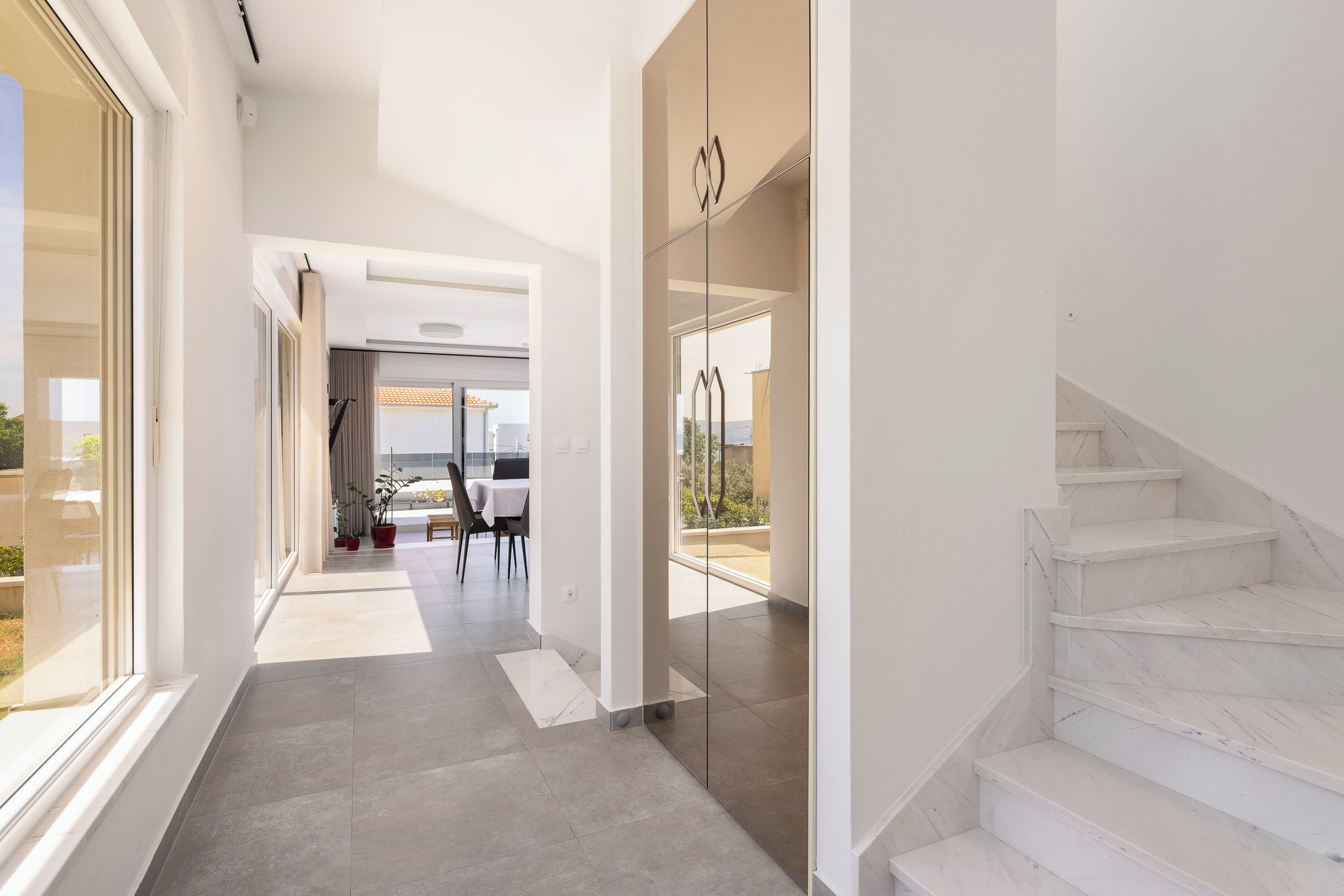 A modern interior with a hallway leading to a dining area and a staircase.