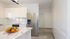 A modern kitchen with white cabinetry, a stainless steel refrigerator, a marble countertop, and a bowl of fruit. - The Adriatic Retreat (Podstrana - Mutogras)