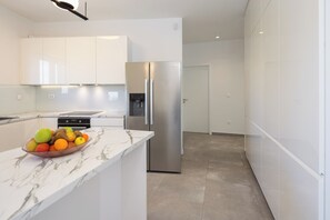 Eine moderne Küche mit weißen Schränken, einem Edelstahlkühlschrank, einer Marmorarbeitsplatte und einer Obstschale.