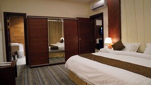 Habitación de hotel con cama, escritorio, espejo y baño visible a través de una puerta abierta.