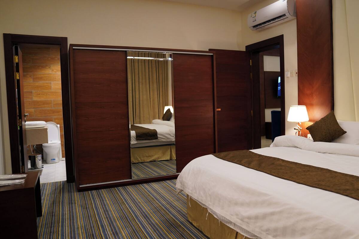 A hotel room with a bed, a desk, a mirror, and a bathroom visible through an open door.