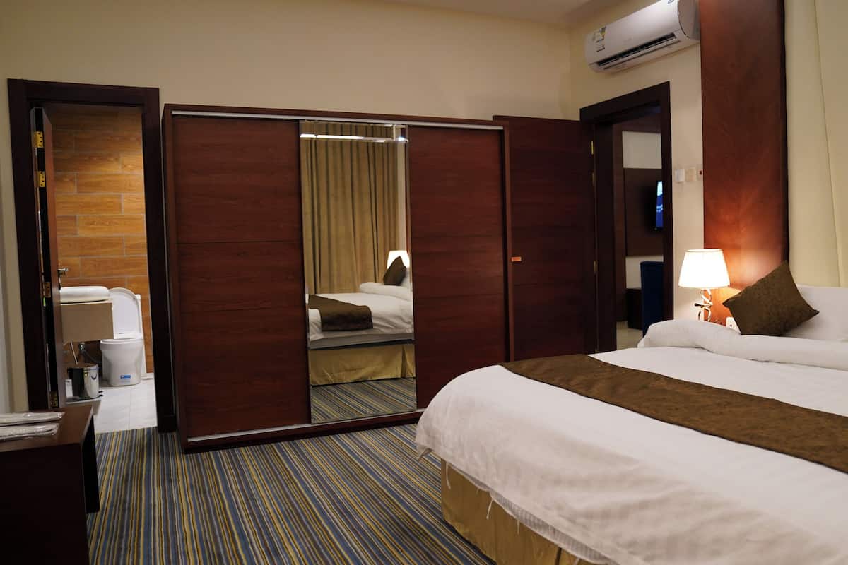 A hotel room with a bed, a desk, a mirror, and a bathroom visible through an open door.