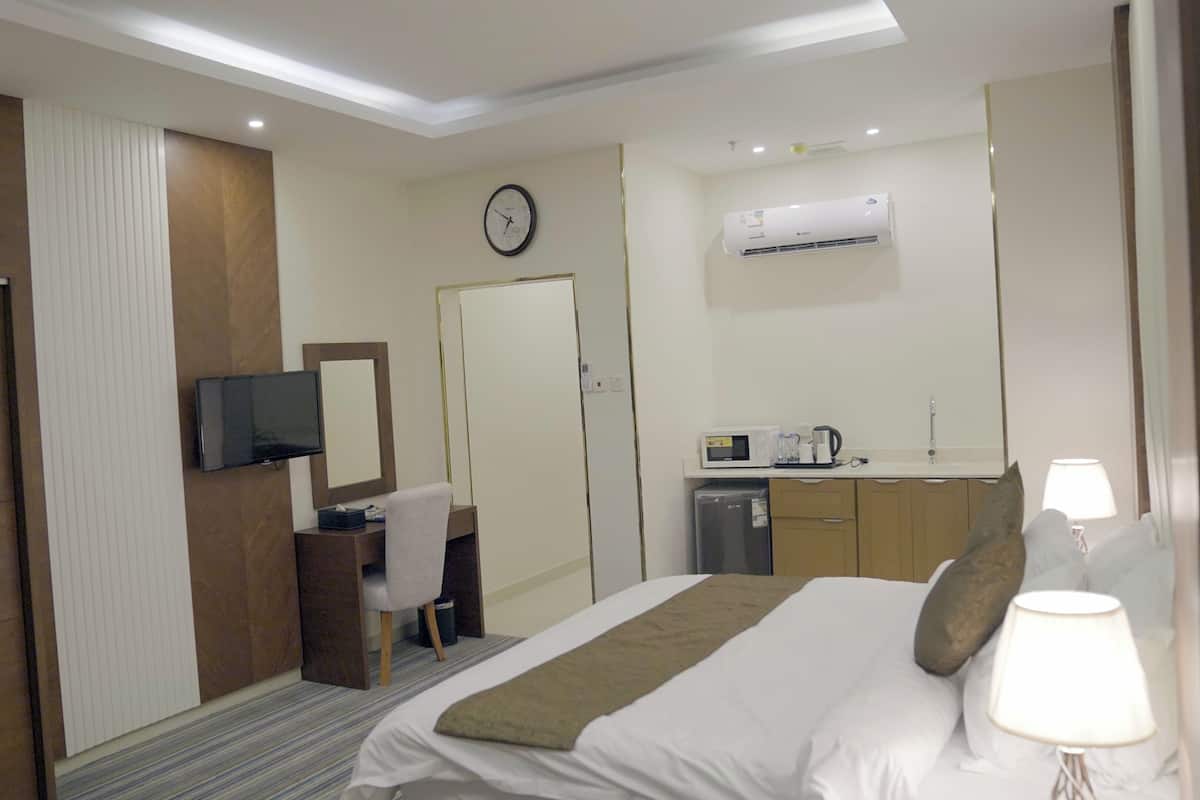 A hotel room with a bed, a desk, a television, a clock, a microwave, and a sink.