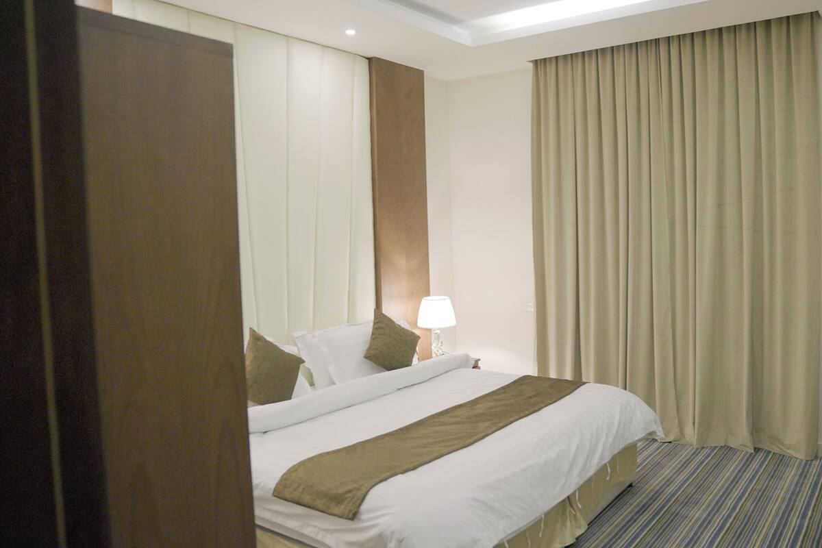 A hotel room with a bed, a desk, a chair, a lamp, and a window with curtains.