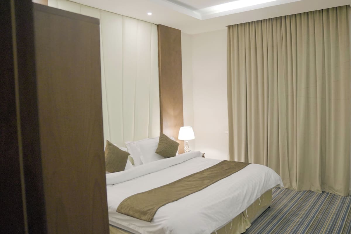 A hotel room with a bed, a desk, a chair, a lamp, and a window with curtains.