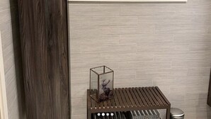 Een badkamer met een houten kolom, een raam met twee potplanten, een prent van een hert en een klein tafeltje met een vuilnisbak.