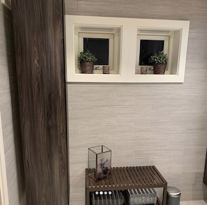Ein Badezimmer mit einer Holzsäule, einem Fenster mit zwei Topfpflanzen, einem Bild von einem Reh und einem kleinen Tisch mit einem Mülleimer.