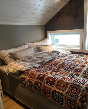 A bedroom with a bed, pillows, a window, and a colorful crocheted blanket. - Cabin in the heart of Sirdal - ski in/ski out, great outdoor area with large jazzuci (Tjørhom)