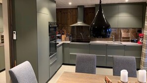 Een moderne keuken met grijze kastjes, een centraal eiland en een eethoek met een tafel en stoelen.