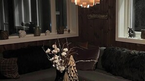 Een gezellige kamer met een donkere bank, een vaas met takken en een raam met gordijnen.