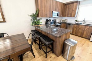 A modern kitchen with wooden cabinets, a granite countertop, a stainless steel sink, and a trash bin. - Welcome to Boise Grove — a thoughtfully designed, modern retreat in one of Boise’s most exciting and fast-growing neighborhoods. Located in Garden City, just steps from greenbelt (Garden City)