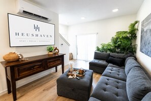 A modern living room with a grey sectional sofa, a wooden console table, and a large framed sign on the wall. - Welcome to Boise Grove — a thoughtfully designed, modern retreat in one of Boise’s most exciting and fast-growing neighborhoods. Located in Garden City, near the greenbelt, E bikes for rent. (Garden City)