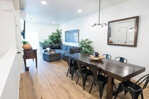 A modern living room with a dining area, a sofa, a coffee table, and a large painting on the wall. - Welcome to Boise Grove — a thoughtfully designed, modern retreat in one of Boise’s most exciting and fast-growing neighborhoods. Located in Garden City, just steps from greenbelt, E bikes for rent (Garden City)