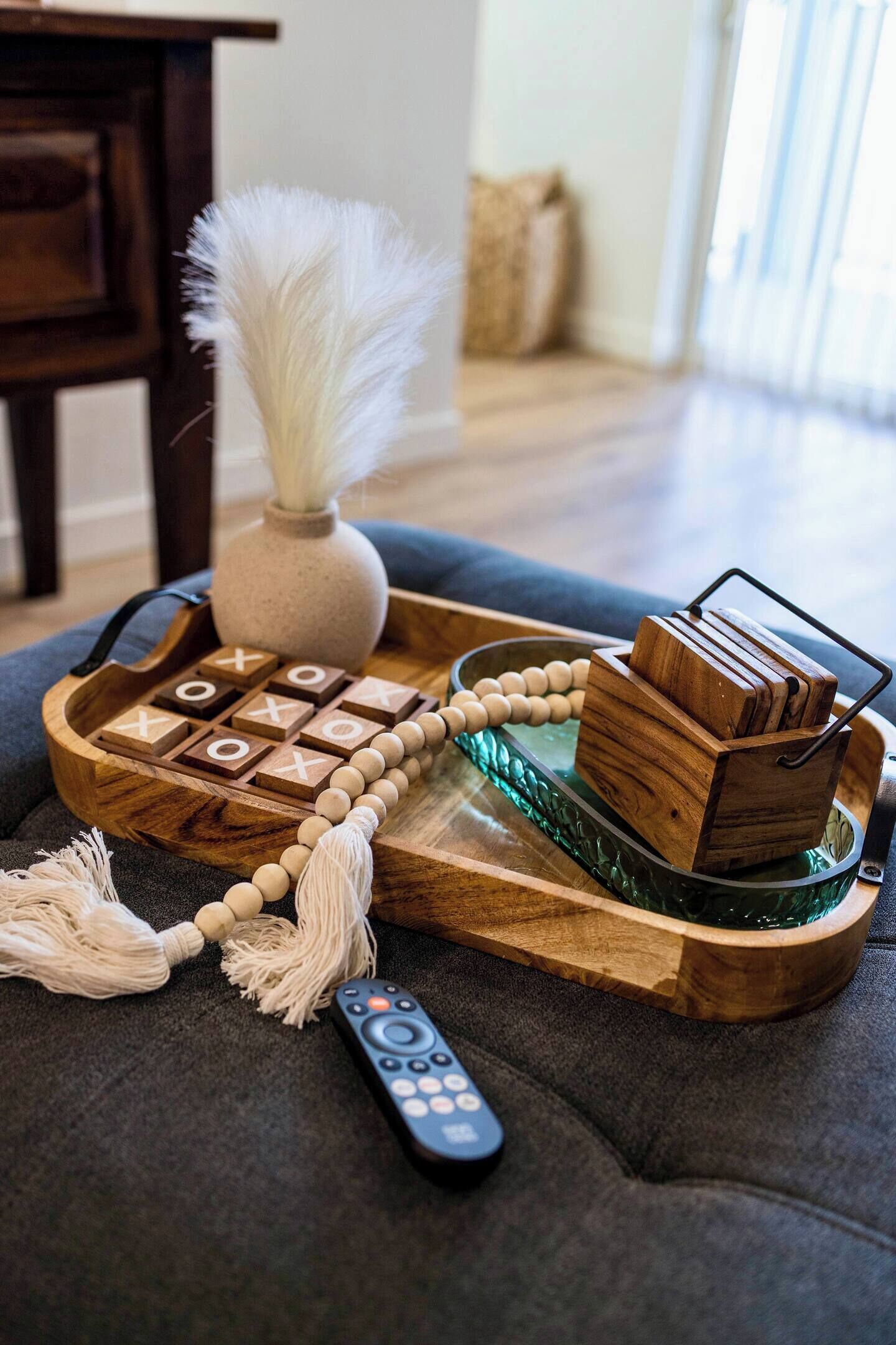 A wooden tray with a wooden telephone, a remote control, and a beaded string.