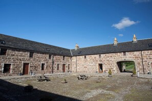 A stone building with a courtyard, stone walls, and a clear sky. - Holstein Cottage The Dairy at Daviot (Inverness)