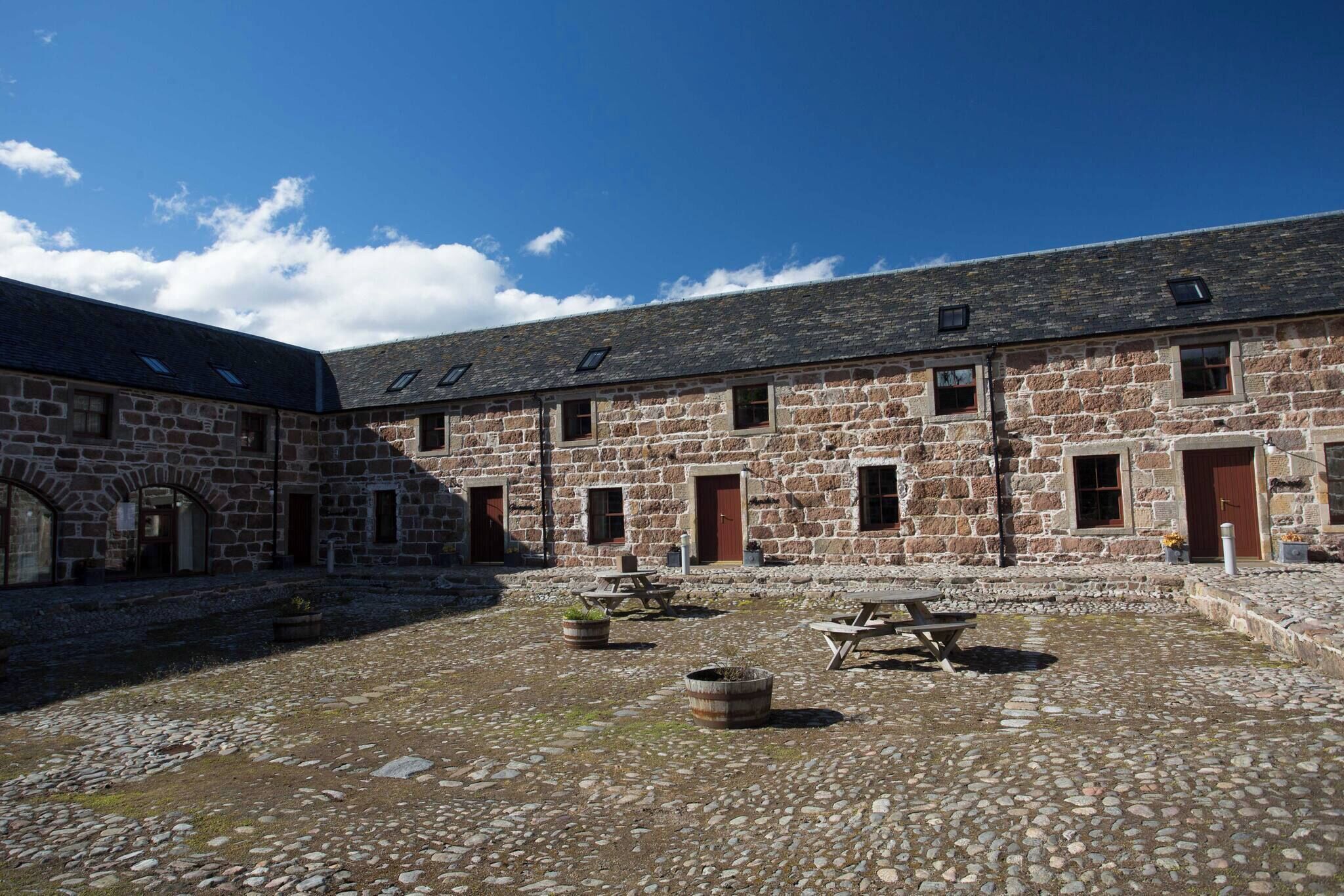 A stone building with multiple windows and doors, a courtyard with stone paving, and outdoor seating areas.