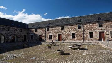 A stone building with multiple windows and doors, a courtyard with stone paving, and outdoor seating areas.