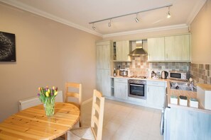 Une cuisine moderne avec des meubles de couleur bois clair, un îlot central et un coin repas comprenant une table et des chaises en bois.