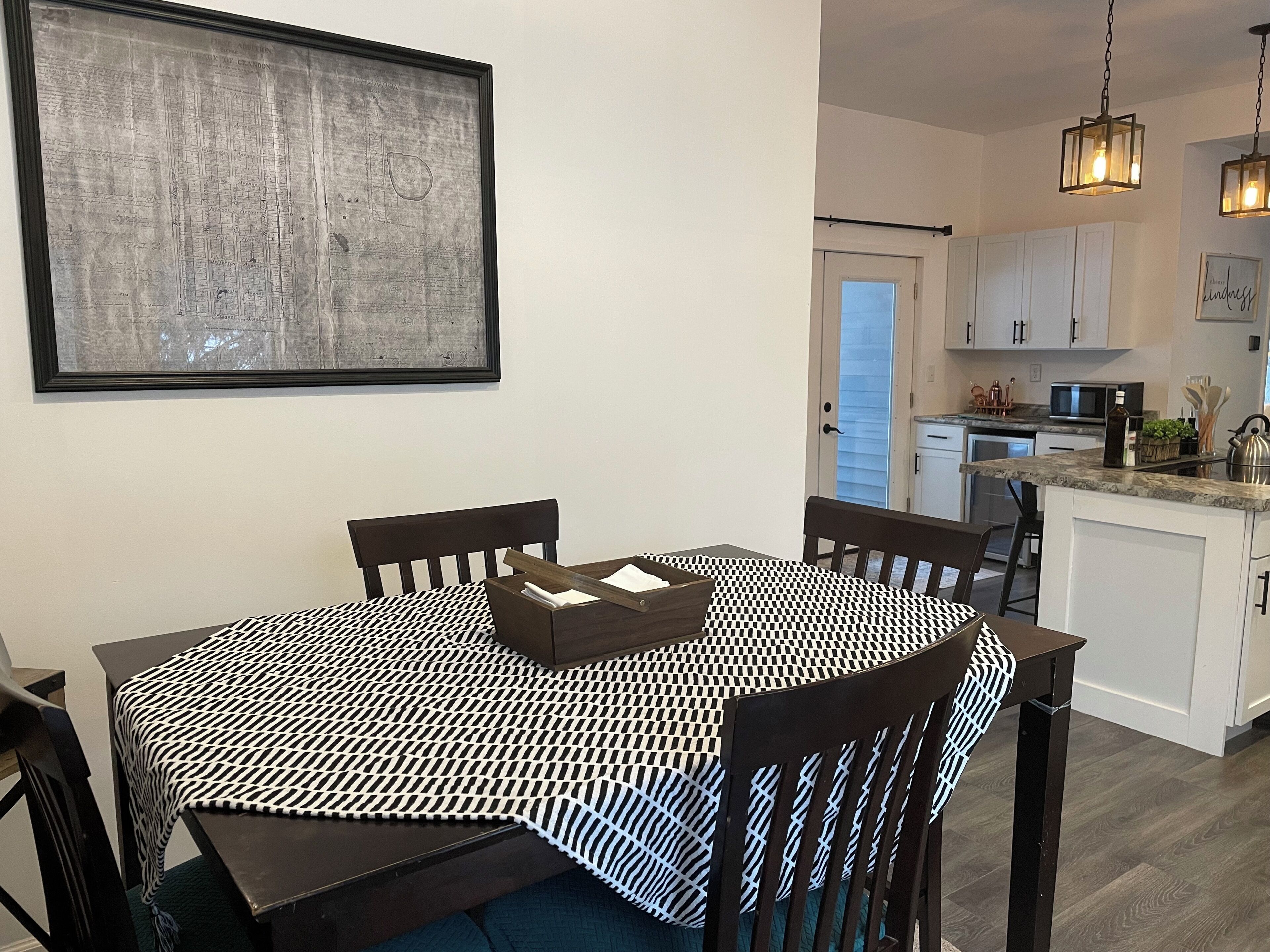 A dining area with a black and white checkered tablecloth, wooden chairs, and a framed map on the wall.