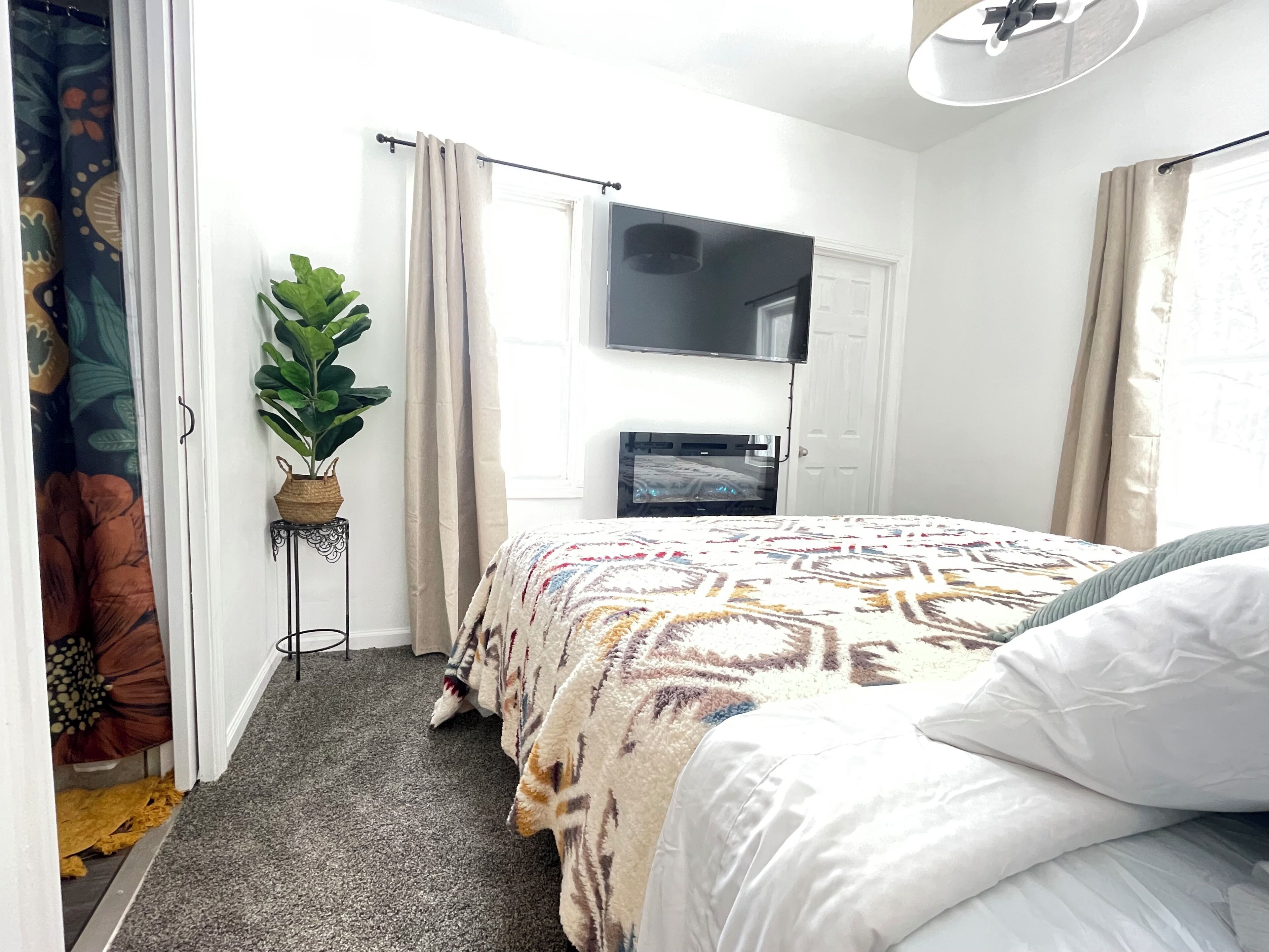 A bedroom with a bed, a TV mounted above it, a potted plant, and a door with a curtain.