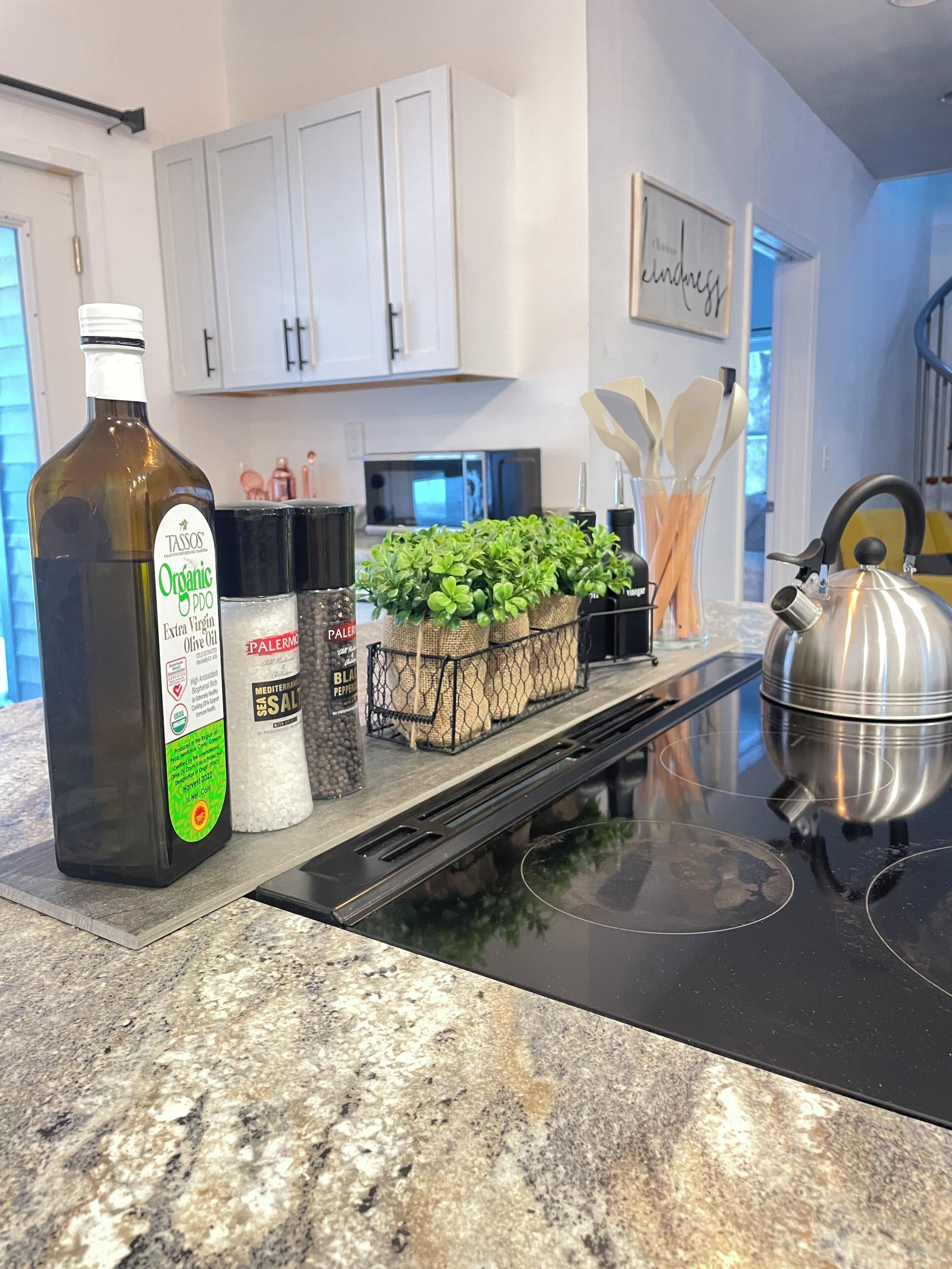 A kitchen with a bottle of organic extra virgin olive oil, a salt shaker, and a tray of herbs on the counter.