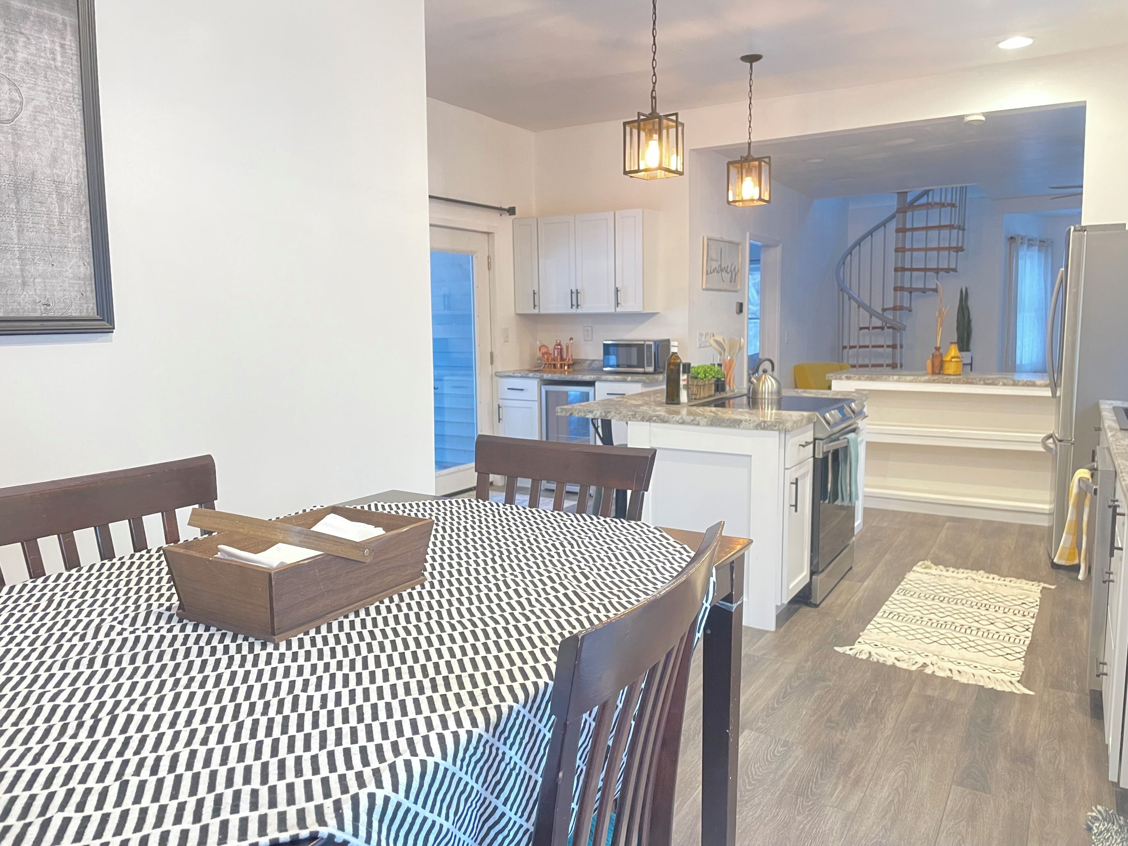 A modern kitchen with white cabinets, a central island, and a dining area with a patterned tablecloth.