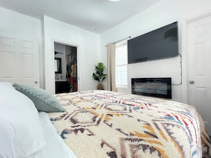 A bedroom with a bed, a TV mounted on the wall, and a door leading to a bathroom. - Enjoyable 3-bedroom cabin with AC in charming Crandon walkingdistanceMetongaLake (Crandon)