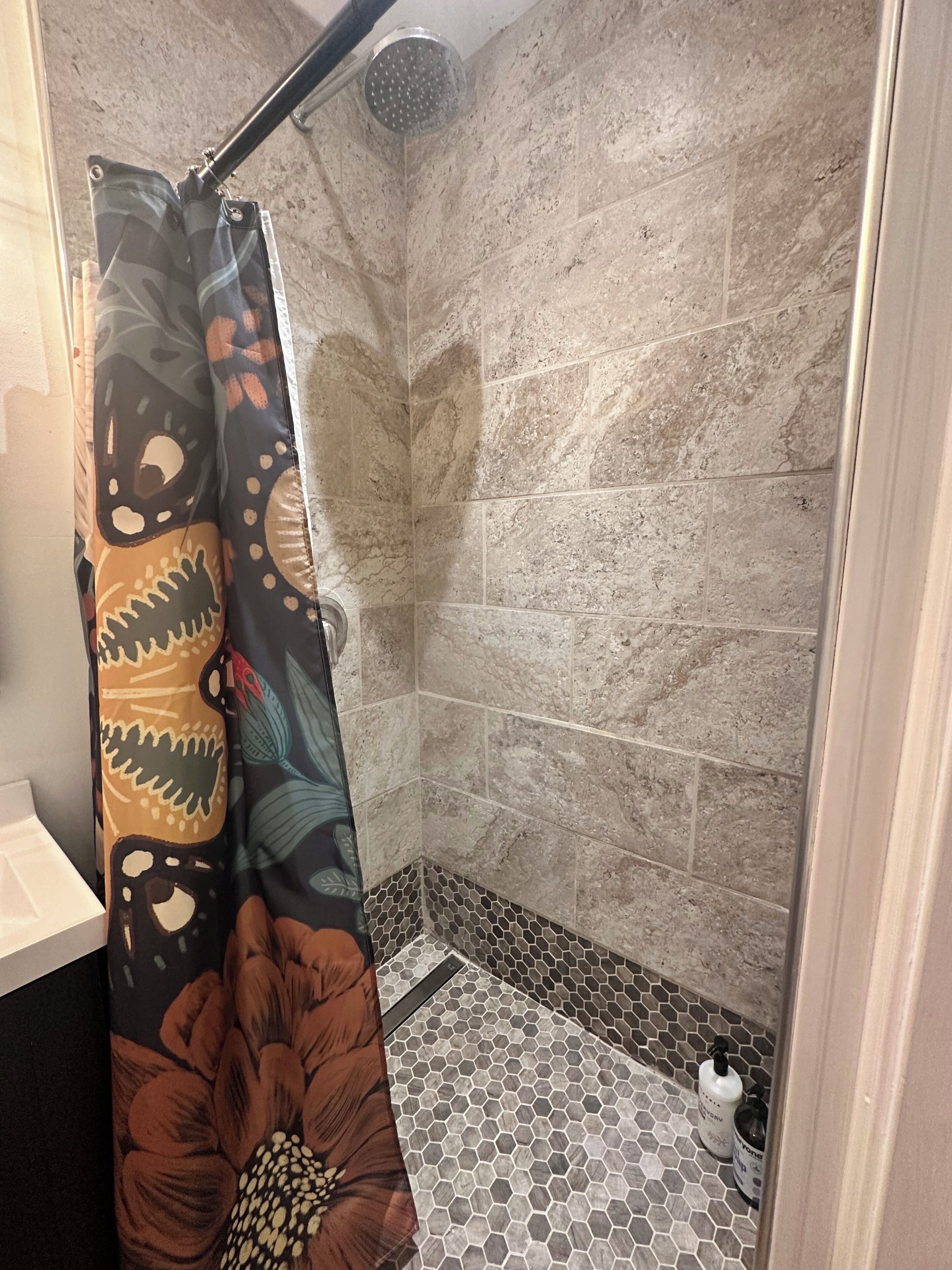 A shower with a patterned curtain, hexagonal tile flooring, and a showerhead.