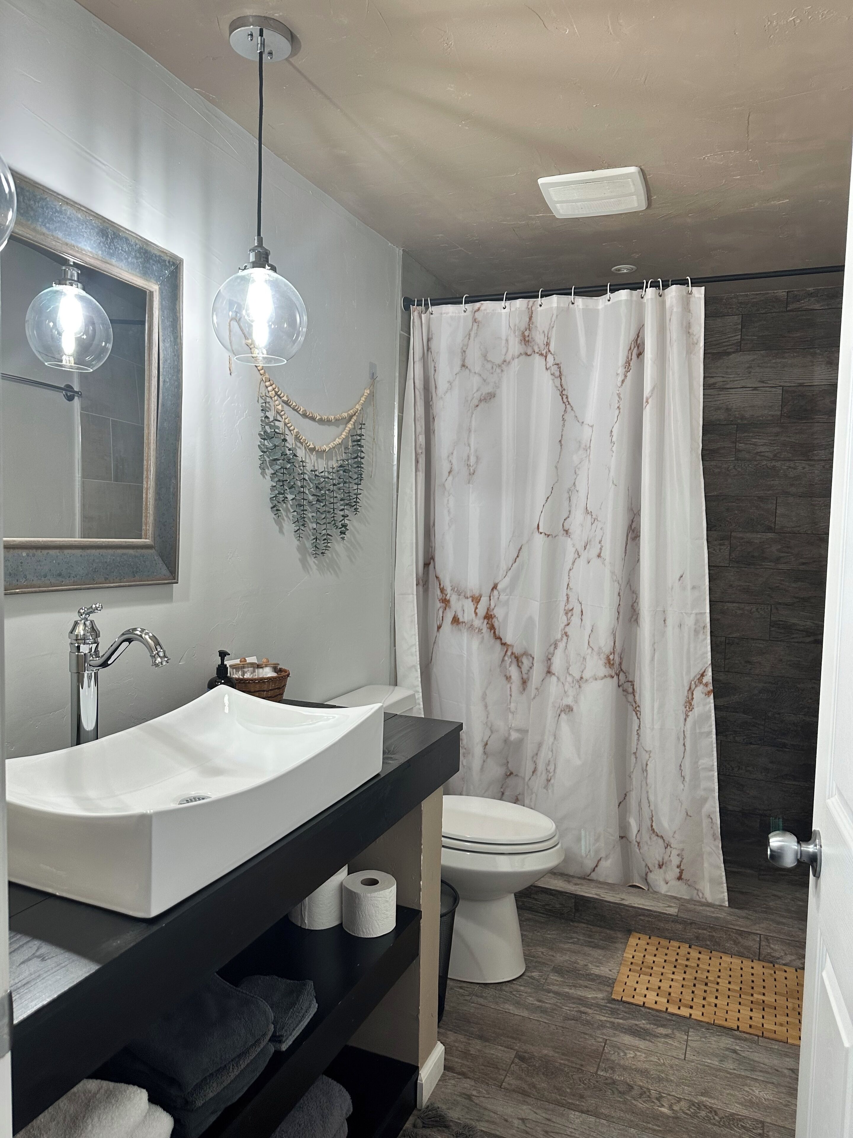 Une salle de bain avec un lavabo blanc, un miroir, un rideau de douche, des toilettes et un plancher en bois.