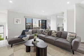 Ein modernes Wohnzimmer mit einem Ecksofa, einem Couchtisch und Blick auf die Skyline durch große Fenster.