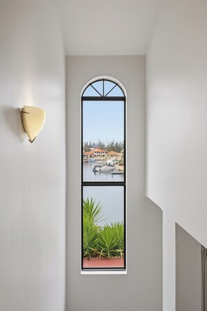 Ein Zimmer mit großem Fenster, einer Wandleuchte und Blick auf ein Gewässer mit Booten.