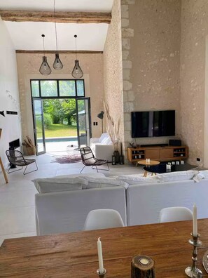 Una sala de estar moderna con sofá, mesa de comedor, televisor y vistas al exterior.