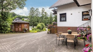 En kullerstensgång som leder fram till ett hus med en trädgård och en utomhusplats med sittmöbler.