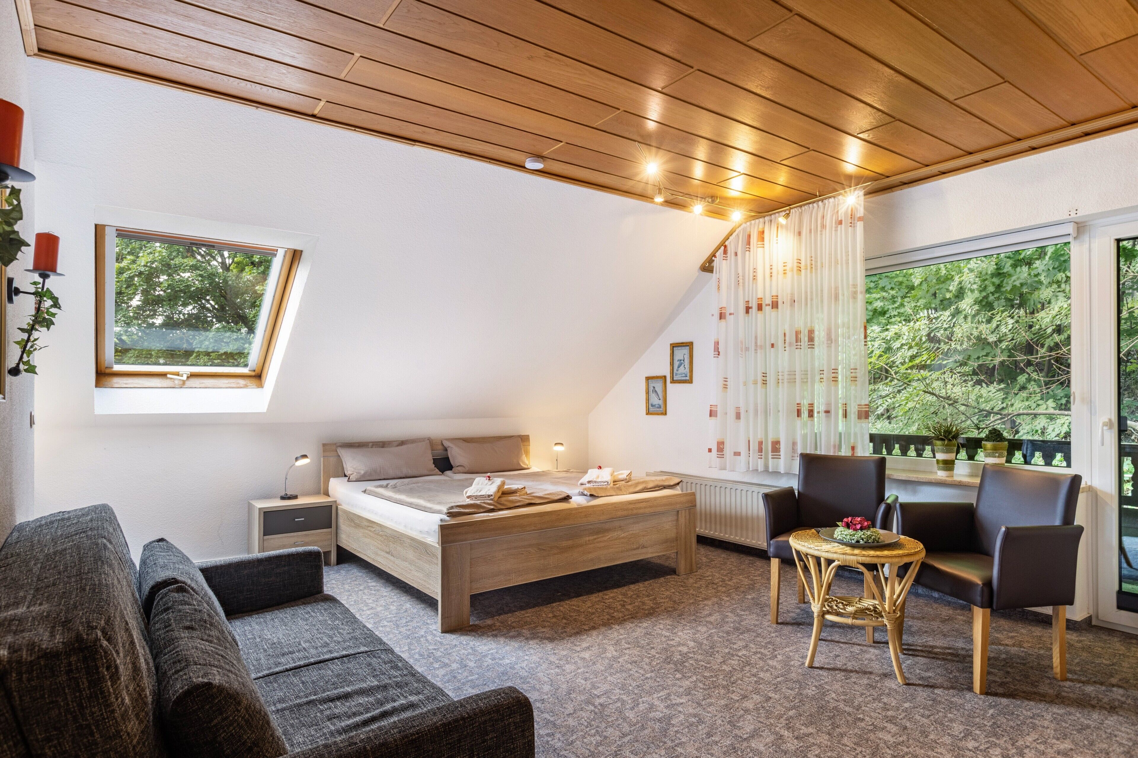 Une chambre à coucher avec un lit, des tables de chevet, une fenêtre, une chaise et une vue sur la verdure.