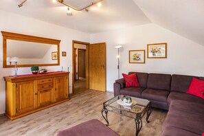 A living room with a wooden cabinet, a glass coffee table, a brown sofa, and a red cushion. - Apartment 'Fewo B' at the Golf Course with Mountain View, Balcony and Wi-Fi (Willingen)