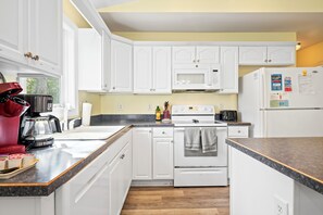 Una cocina con armarios blancos, un microondas, una estufa y un refrigerador.